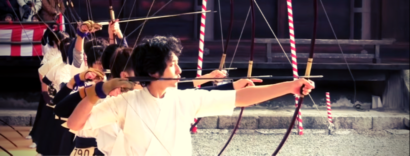 Japanese archers are standing in a line and shooting a bow and arrow 